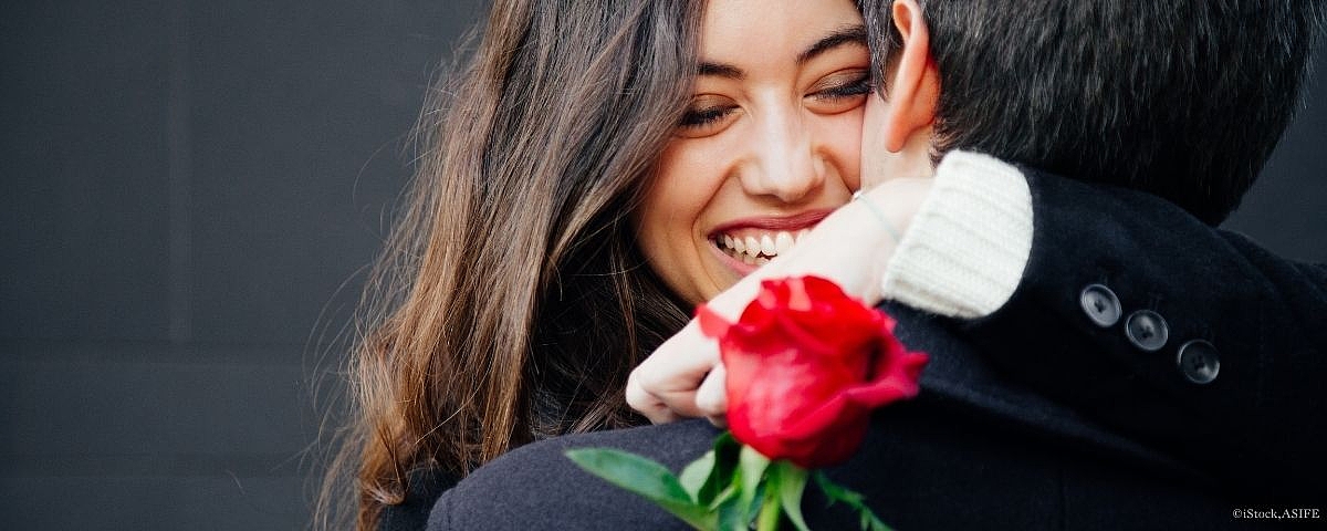 Schloss Wackerbarth Woman hugs a person warmly and smiles while holding a red rose in her hand.