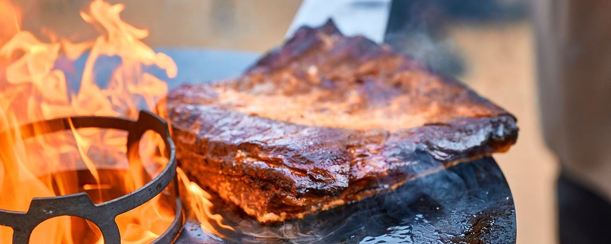 Schloss Wackerbarth Large pieces of meat are grilled over an open fire, with a crispy crust and visible flames.