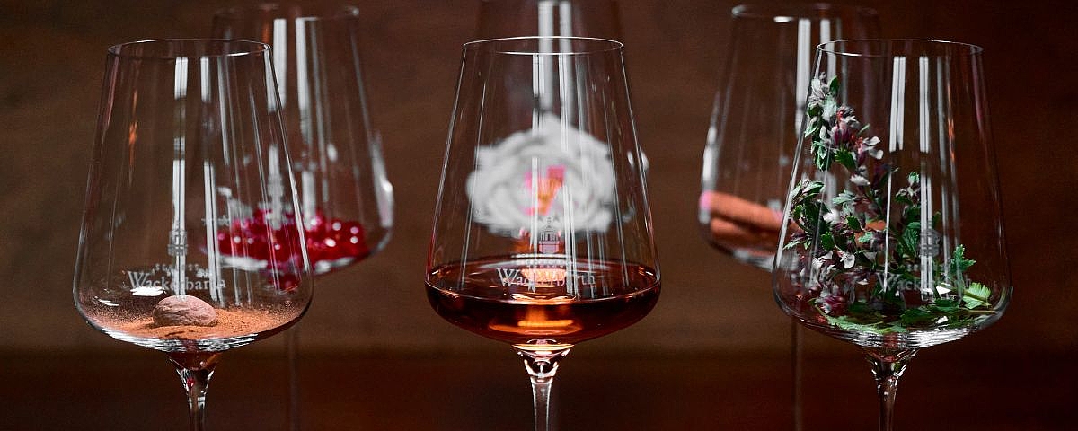 Schloss Wackerbarth  Six elegant wine glasses with red wine, rosé and white wine against a dark background, stylishly illuminated.